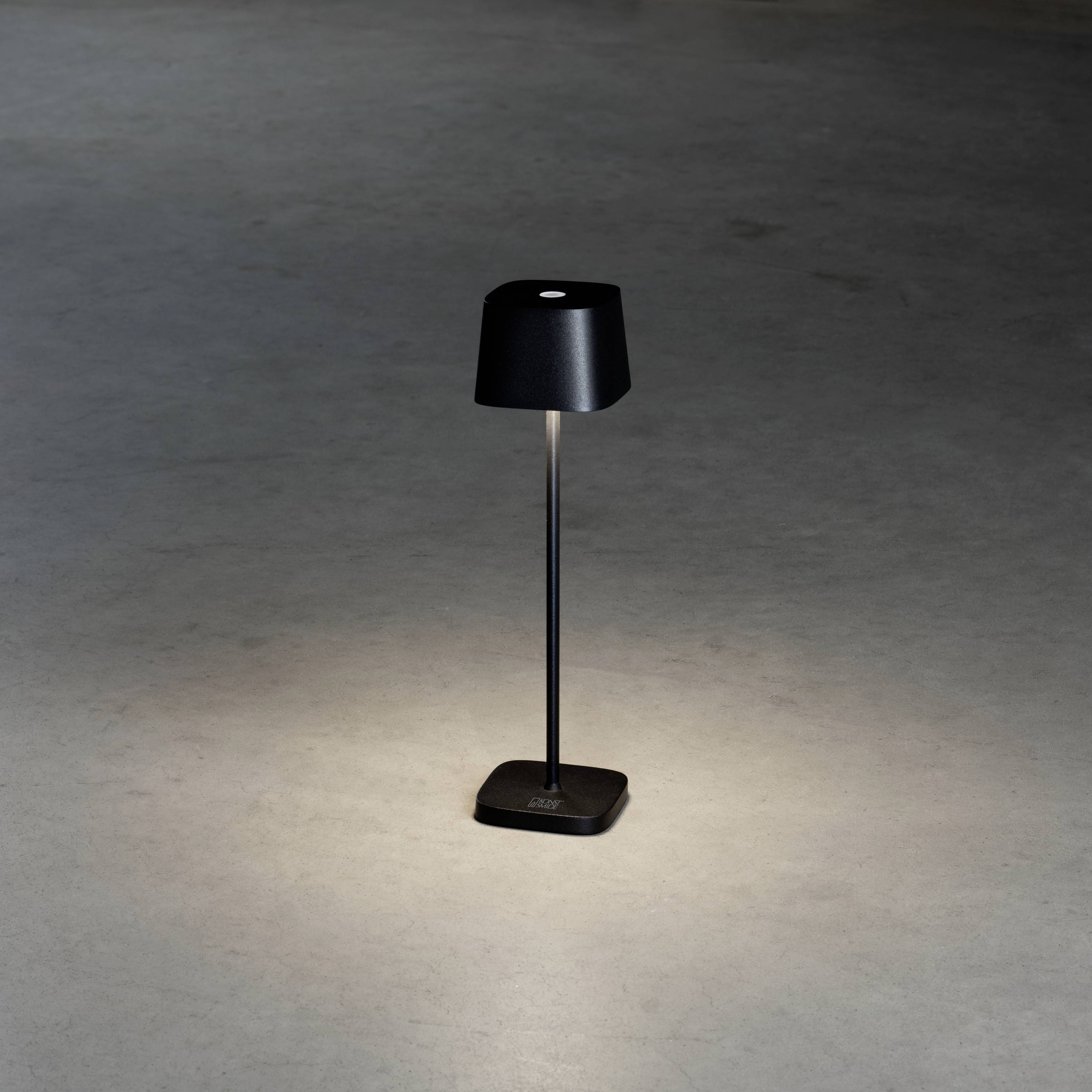 Une lampadaire élancé et noir éclaire dans une pièce sombre, créant un cercle lumineux sur le sol.