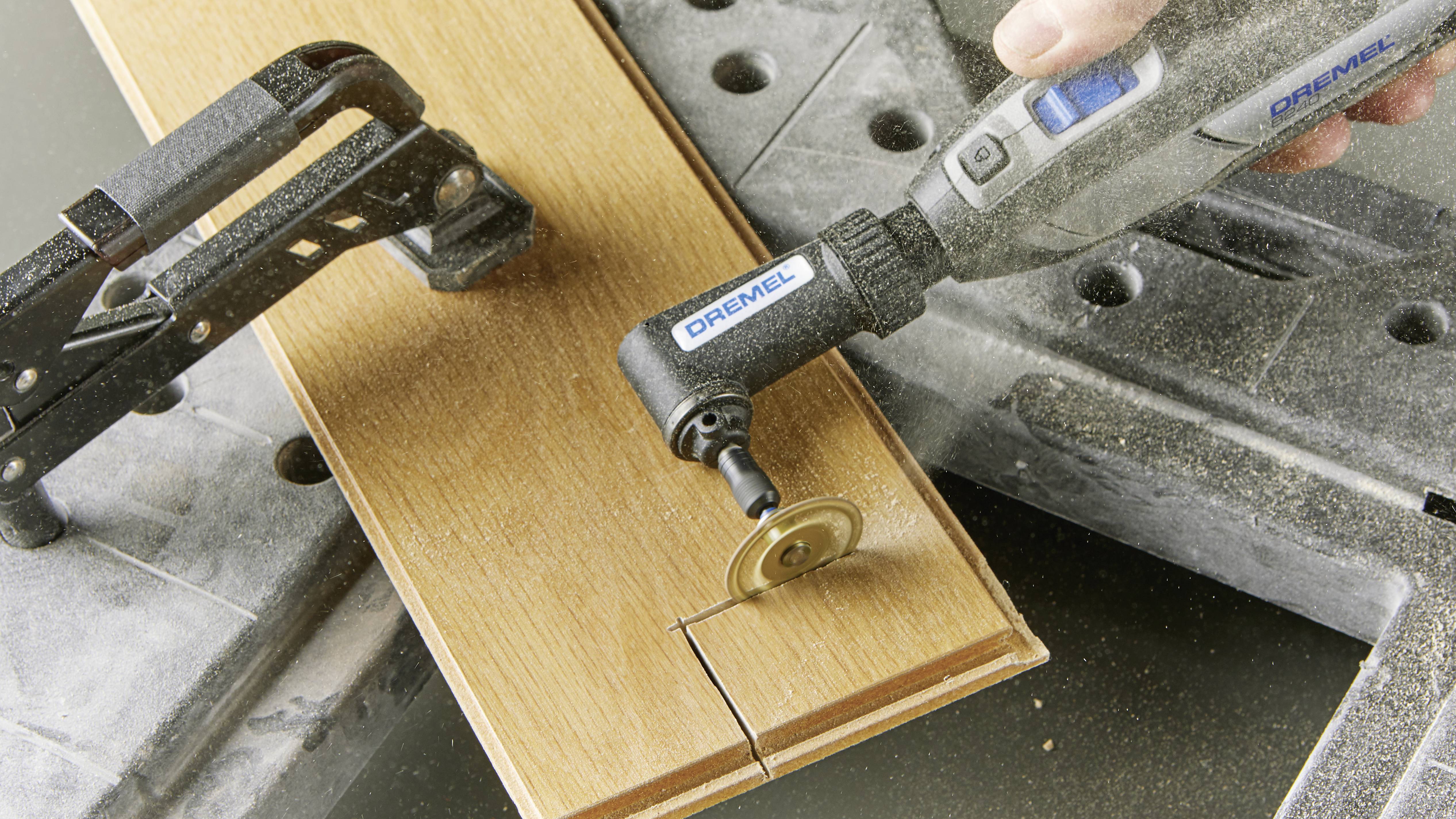 Une défonceuse électrique portable coupe une planche de bois maintenue par un serre-joint. Des particules de sciure s'élèvent pendant la coupe.