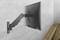 Un moniteur noir est monté sur un bras articulé contre un mur gris. Un bureau en bois se trouve à côté.