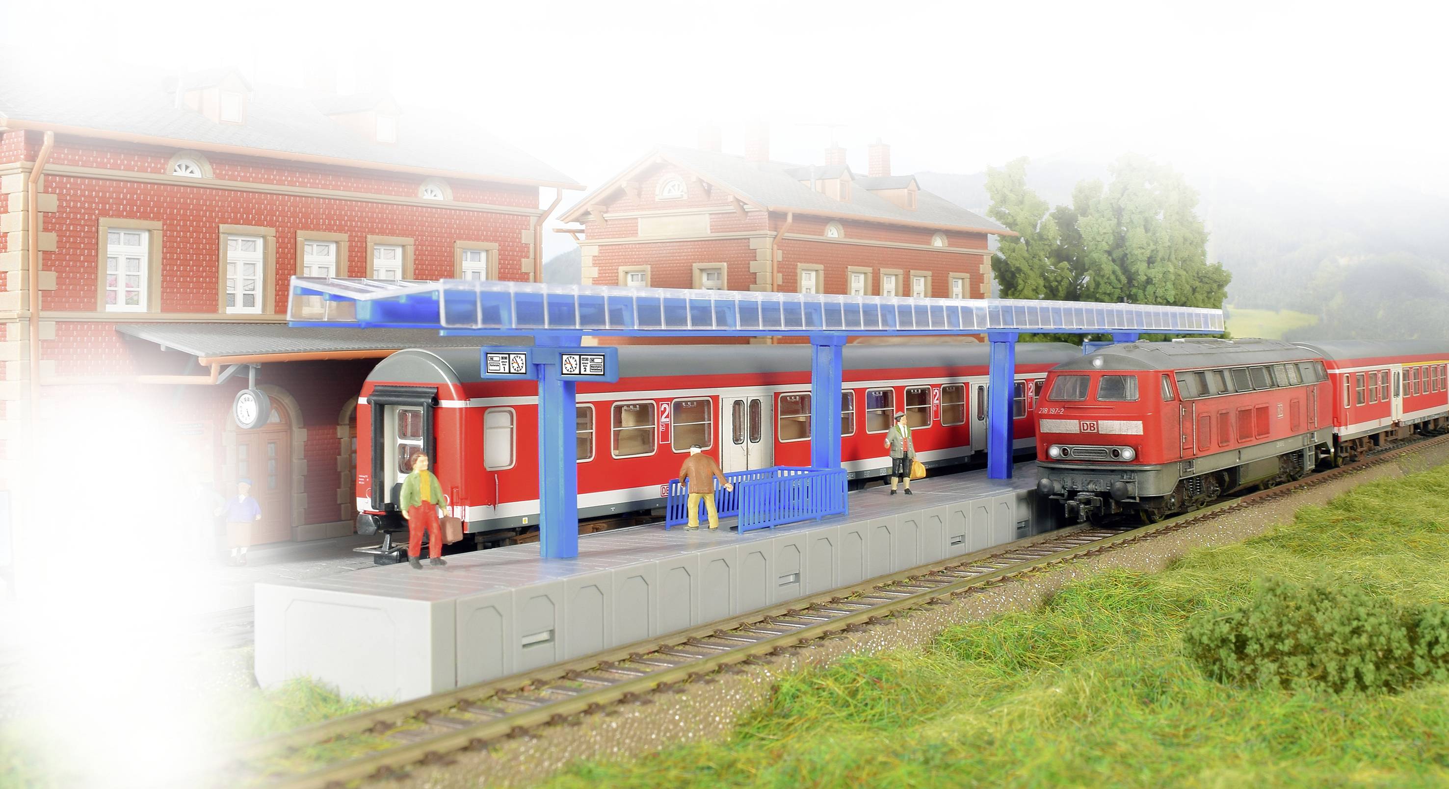 Un train rouge est arrêté en gare, entouré de bâtiments et de passagers. Le train présente des détails bleus et est partiellement enveloppé de brume.