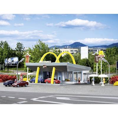 Une maquette d'un restaurant McDonald's avec trois voitures et des figurines devant, entourée d'arbres et de montagnes en arrière-plan.