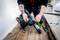 Une personne tient une perceuse verte sur un plancher en bois. La perceuse est sécurisée, et la personne a des tatouages sur le bras.