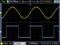 Un oscilloscope affiche deux formes d'ondes : en haut, une onde sinusoïdale jaune et en bas, une onde carrée bleue. Échelle principale : 200 microsecondes par division.