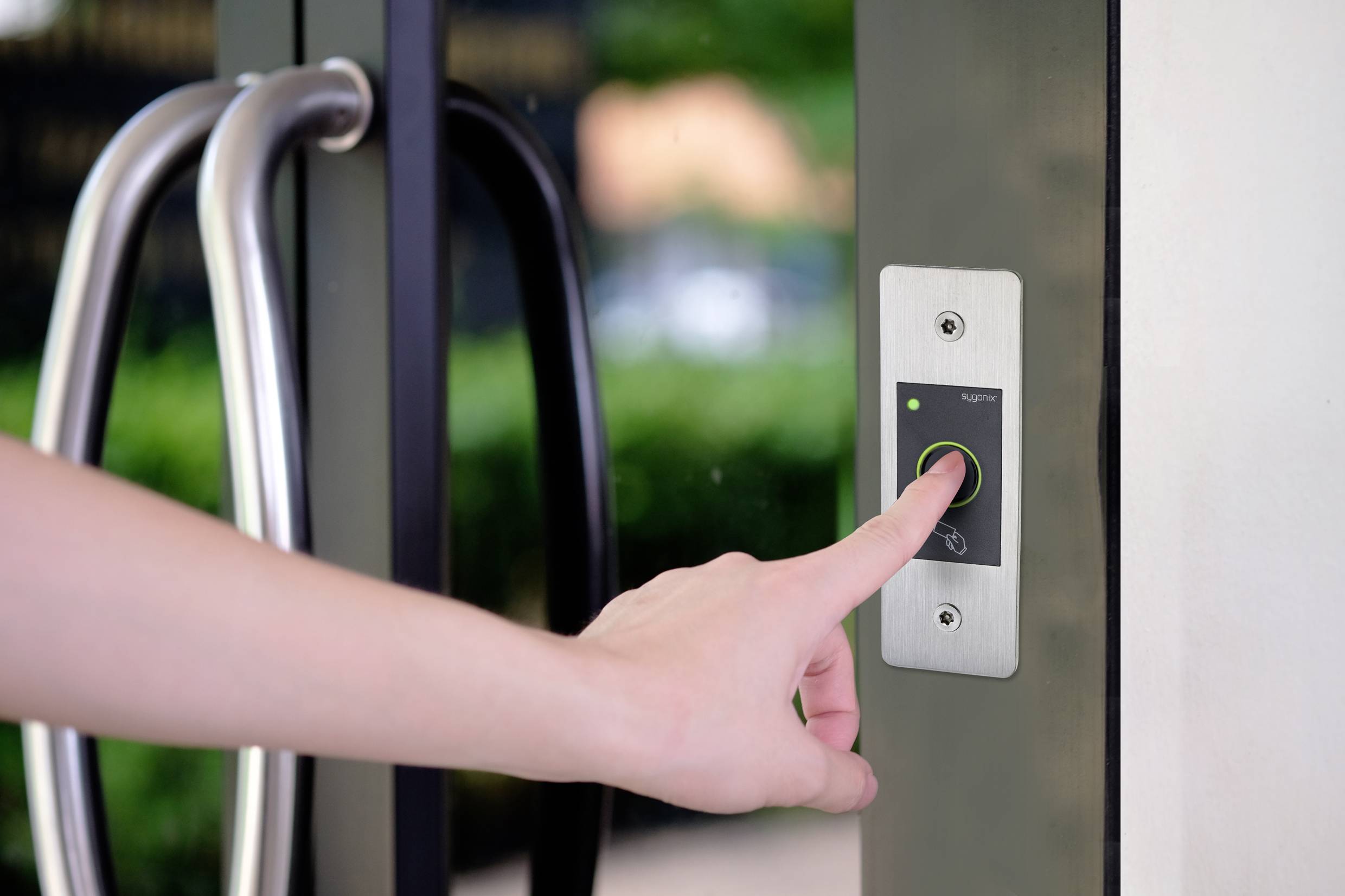 Une main appuie sur un bouton d'un panneau de contrôle d'accès à côté d'une porte vitrée pour ouvrir la porte.