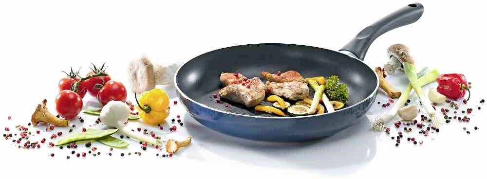 Une poêle noire contenant de la viande rôtie et des légumes tels que des courgettes, des poivrons et du brocoli, entourée de tomates fraîches et de champignons.