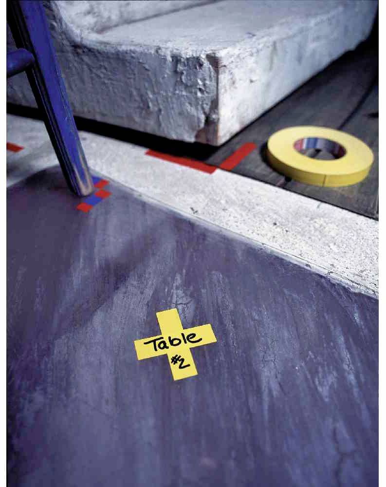 Une bande adhésive jaune au sol portant l'inscription 'Table #2' indique un marquage devant une marche d'escalier. Une autre bande jaune est posée à côté.