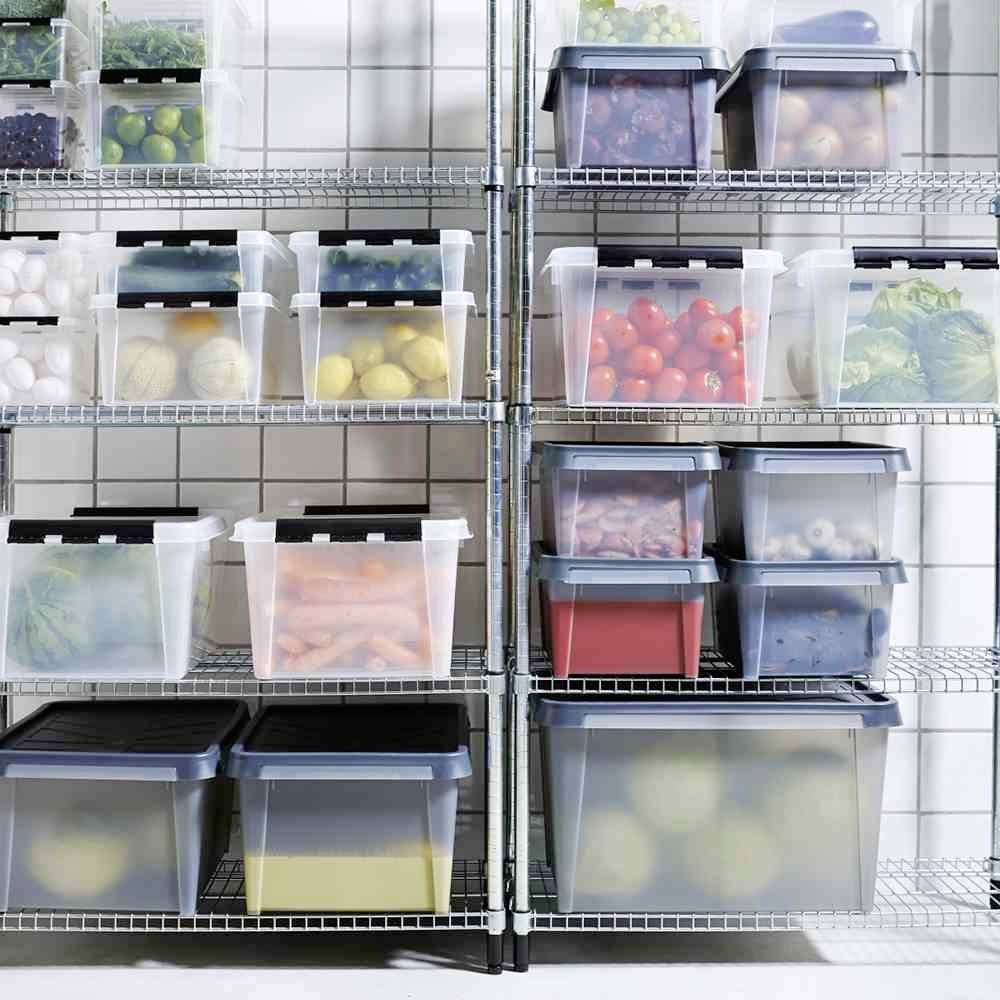 Plusieurs étagères garnies de boîtes en plastique transparentes remplies de divers aliments, dont des légumes, des fruits et des œufs, dans un garde-manger.