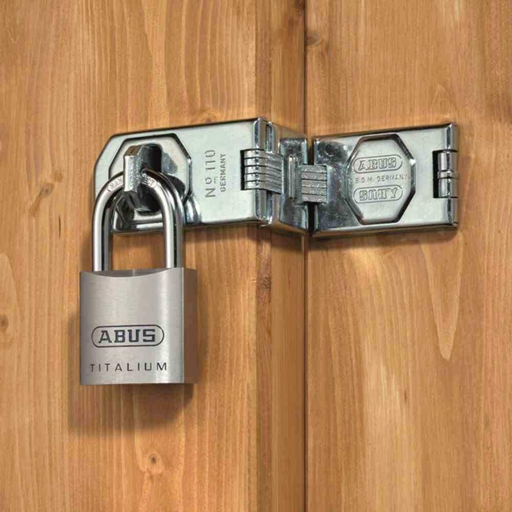 L'image montre un cadenas argenté de la marque 'ABUS Titalium' sur un cabanon en bois. Le cadenas sécurise la porte du cabanon.