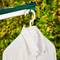 Une chemise blanche est suspendue à un cintre sur une corde à linge devant un fond de buissons verts.