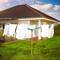 Une araignée à linge verte se dresse dans le jardin d'une maison moderne, garnie de vêtements blancs sous un ciel bleu parsemé de nuages.