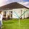 Une femme se tient dans un jardin devant une maison moderne et observe un parasol vert sur la pelouse.