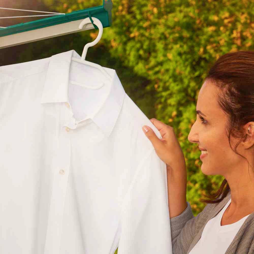 Une personne retire une chemise blanche d'une corde à linge. Des plantes vertes sont visibles en arrière-plan.