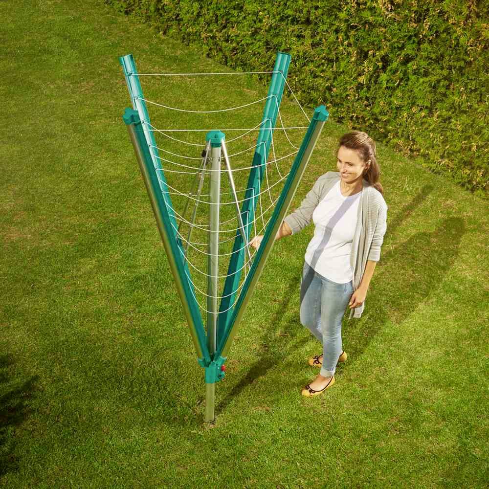 Une femme se tient dans le jardin à côté d'un séchoir à linge vert ouvert, avec plusieurs cordes, prête à étendre son linge.