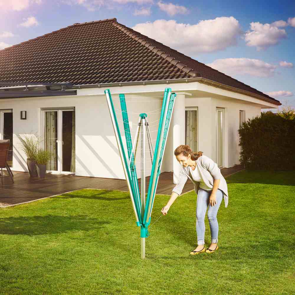 Une femme installe un étendoir à linge dans le jardin devant une maison individuelle moderne sous un ciel bleu.