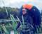 Un homme vêtu de tenue de pêche se tient dans un lac, portant un gilet de sauvetage gonflable sur le dos, avec des roseaux et des arbres en arrière-plan.