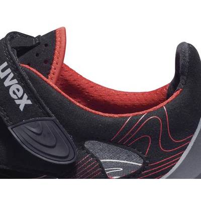 Une chaussure de sport noire avec des accents rouges et une fermeture velcro. La chaussure présente des lignes arrondies sur le côté.