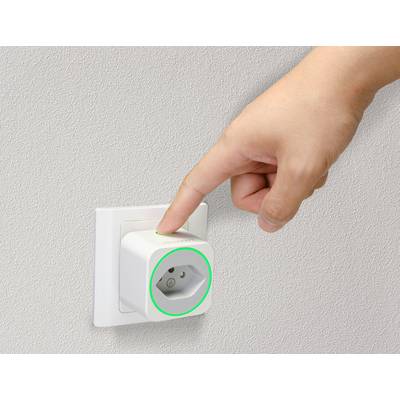 Une main appuie sur un adaptateur de prise intelligente connecté à une prise murale. Un anneau lumineux vert indique l'état de fonctionnement.