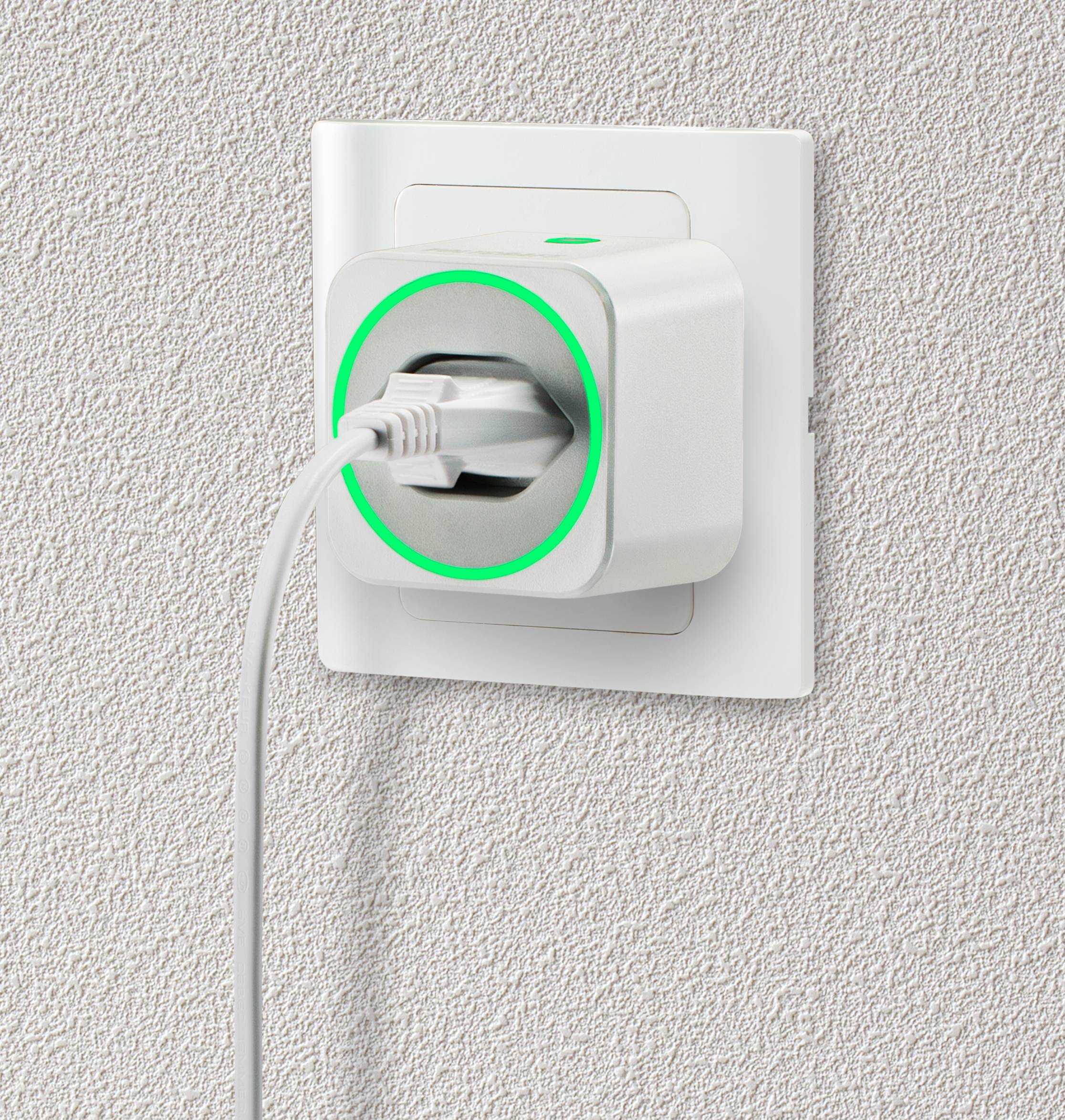 Une prise blanche avec un anneau LED vert est branchée dans une prise murale sur un mur structuré, symbolisant un flux électrique actif.
