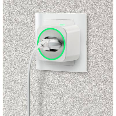 Une prise blanche avec un anneau LED vert est branchée dans une prise murale sur un mur structuré, symbolisant un flux électrique actif.