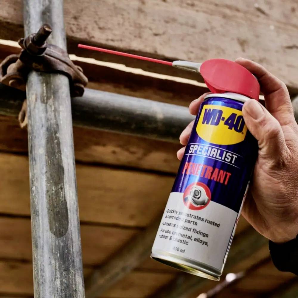 Une main pulvérise un spray dégraissant multifonction WD-40 Specialist avec un petit tube rouge sur une barre métallique pour la lubrifier.