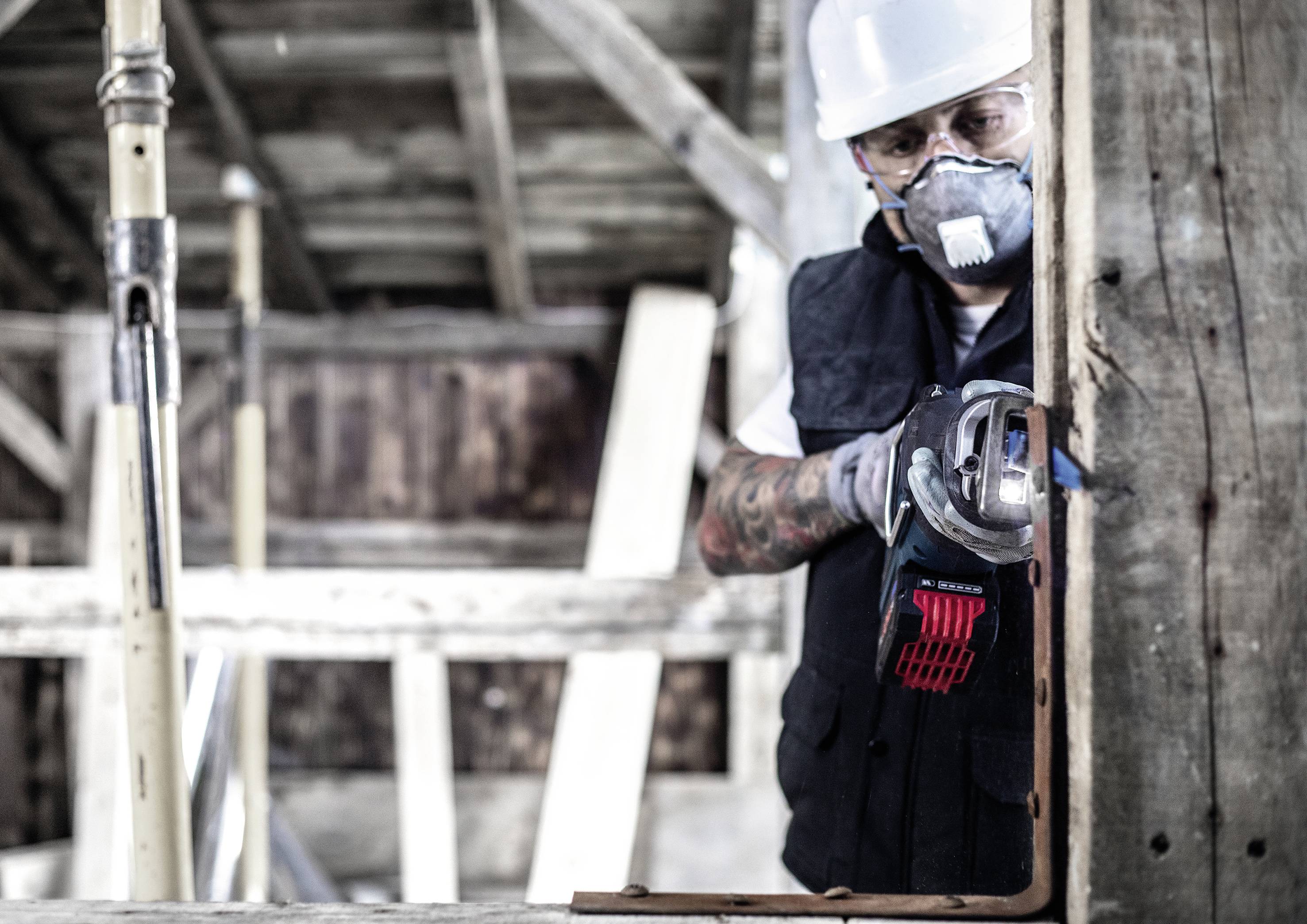 Une personne en tenue de protection utilise une scie électrique pour travailler le bois sur un chantier de construction.