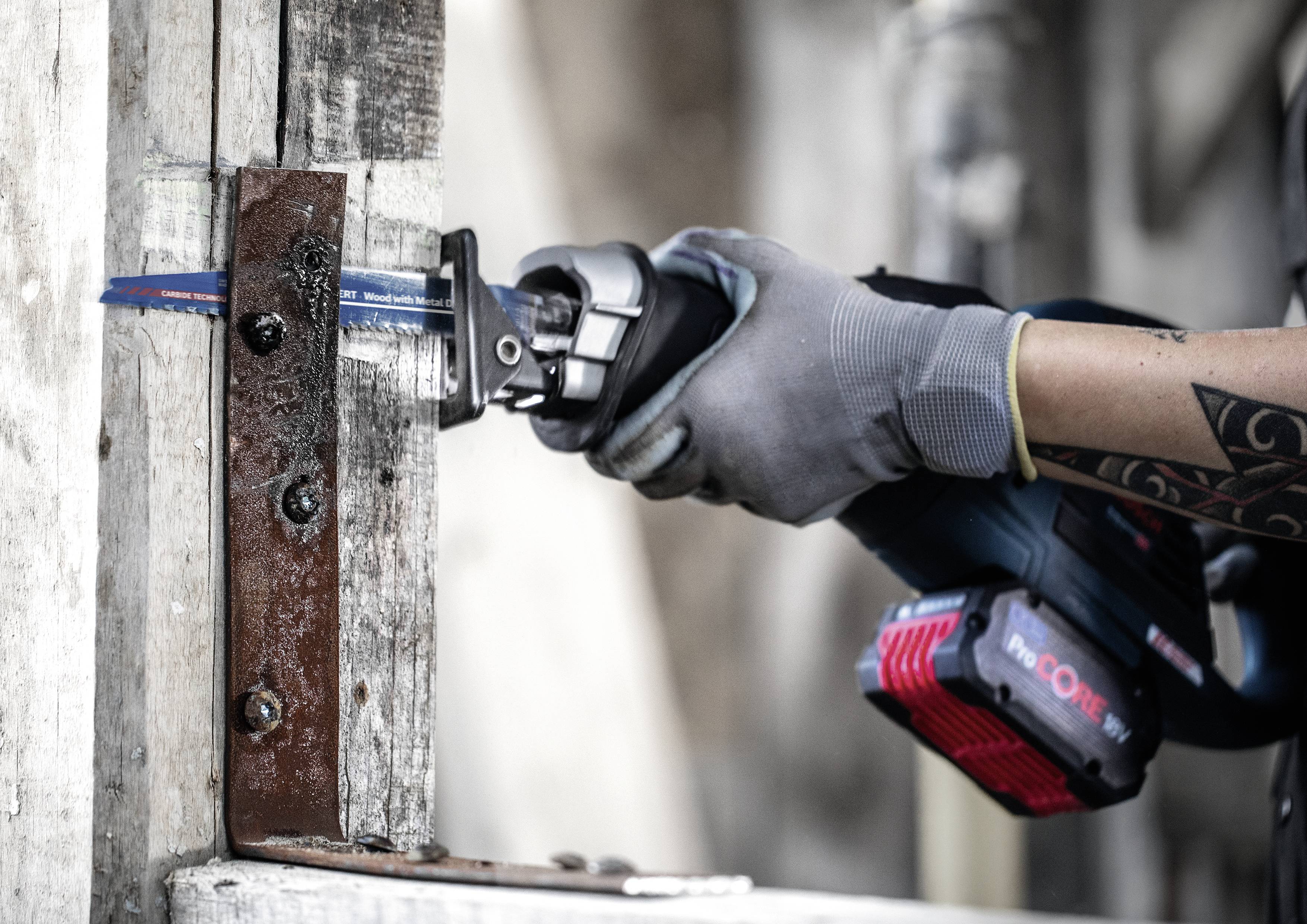 Une personne scie un morceau de métal fixé à une poutre en bois à l'aide d'une scie sauteuse électrique.