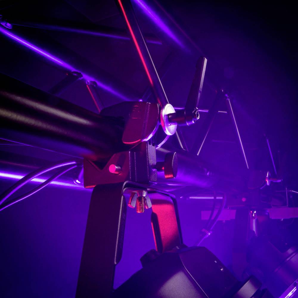 Vue sur une scène avec un éclairage violet et des projecteurs montés sur une structure métallique. Équipement technique pour des performances scéniques.