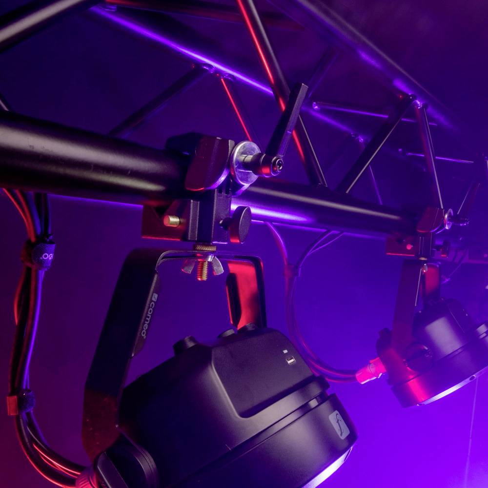 Des projecteurs de scène suspendus à des perches en lumière violette, prêts pour un événement en direct ou une représentation.