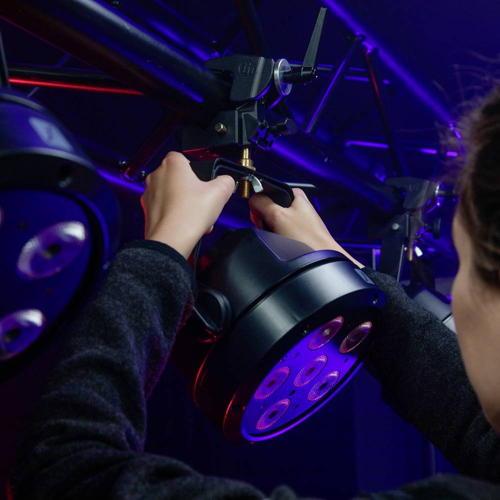 Une personne règle un dispositif d'éclairage dans une pièce baignée de lumières bleues et rouges, créant une ambiance particulière.