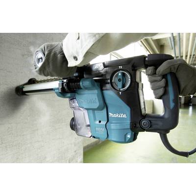 Une personne fore un mur en béton avec un marteau-perforateur bleu équipé d'un filtre HEPA.