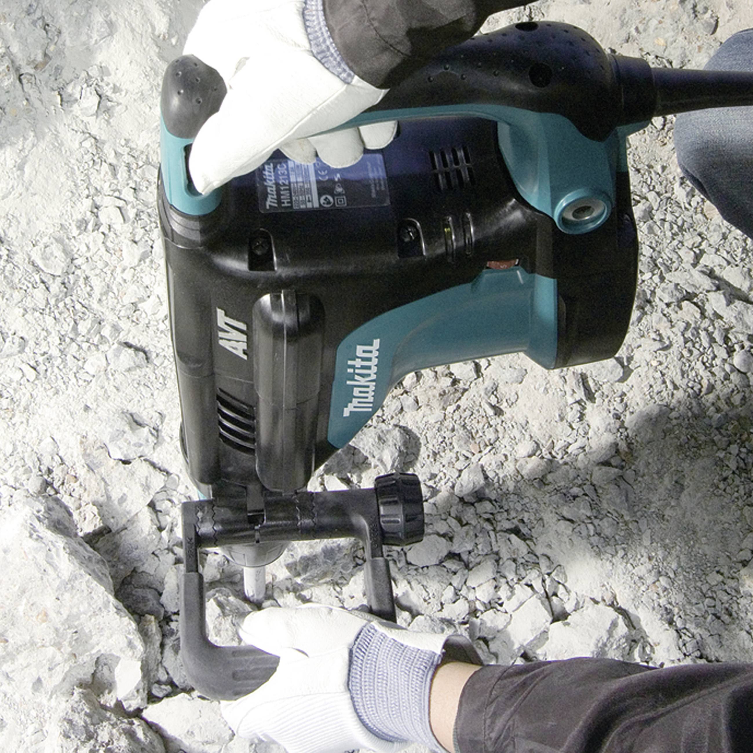 Une personne portant des vêtements de travail utilise un marteau-piqueur sur une surface en béton.