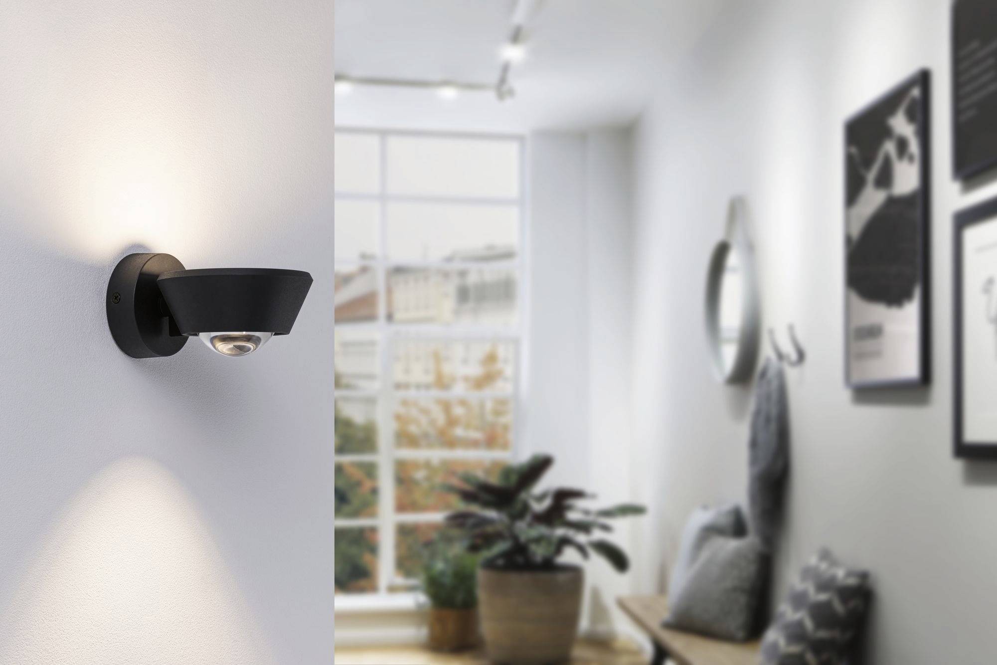 Un luminaire moderne éclaire un couloir lumineux avec des plantes et des tableaux aux murs. Une grande fenêtre se trouve en arrière-plan.