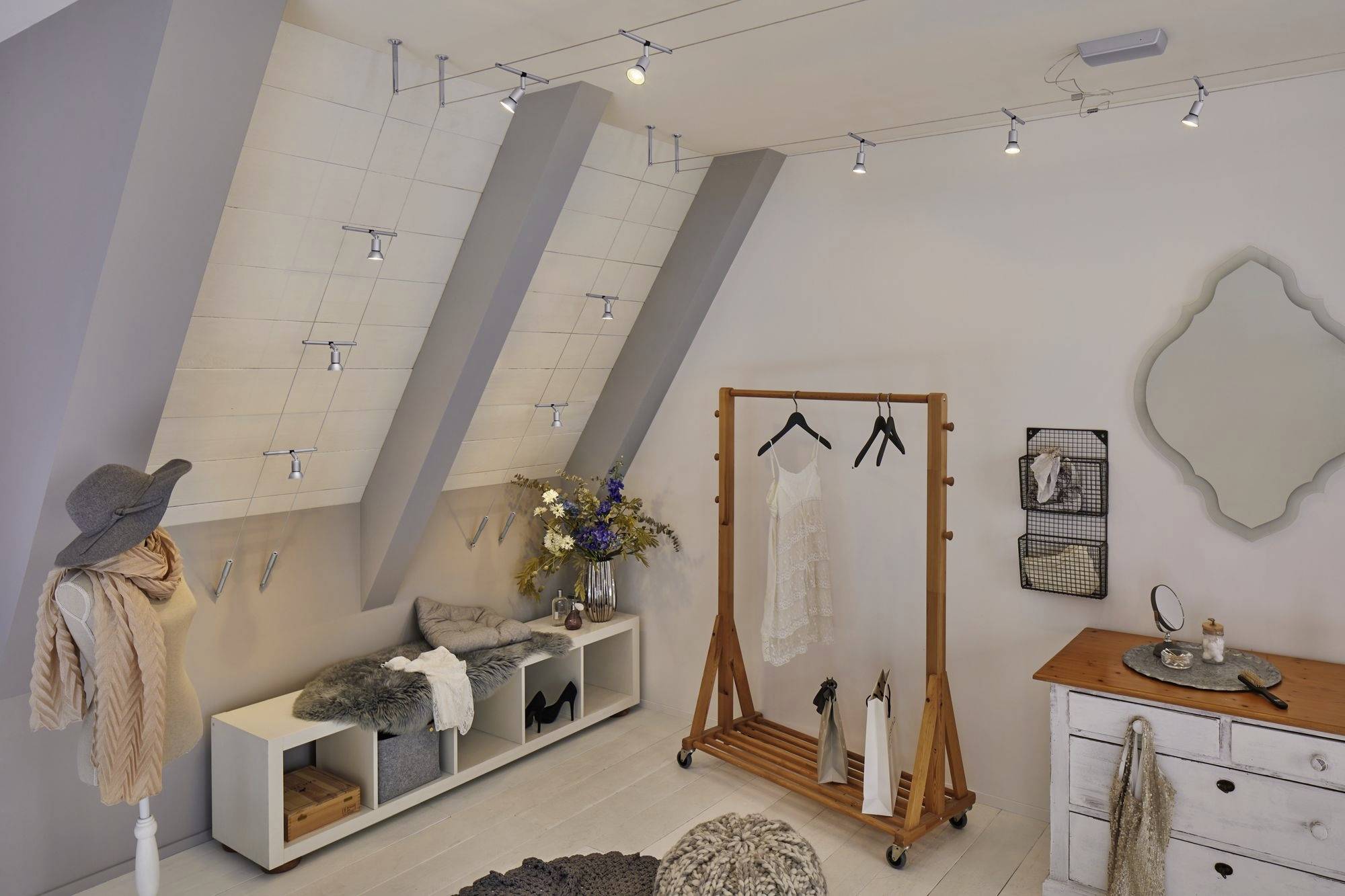 Vestiaire moderne avec plafond en pente, vêtements élégants, miroir décoratif mural, portant et éclairage élégant.