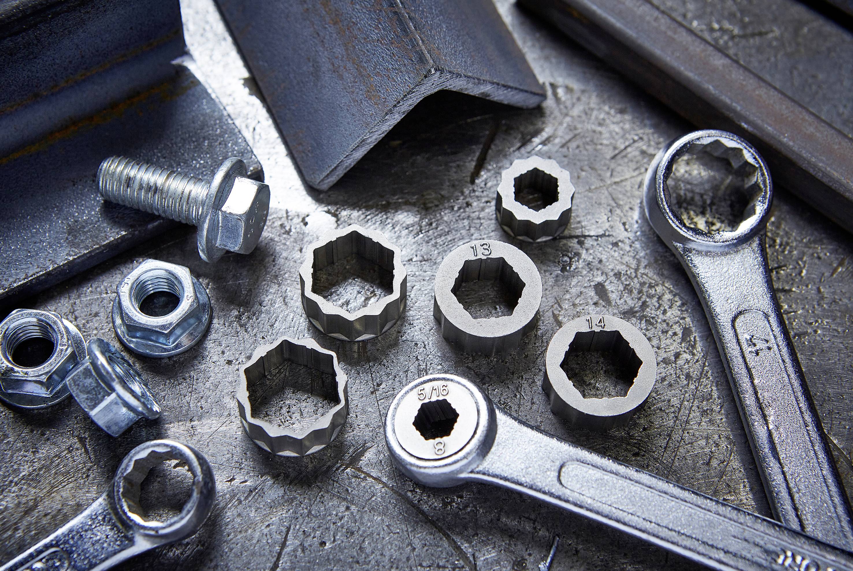 Divers outils et pièces de visserie sur une surface métallique, incluant des clés à molette, des clés hexagonales et des vis.