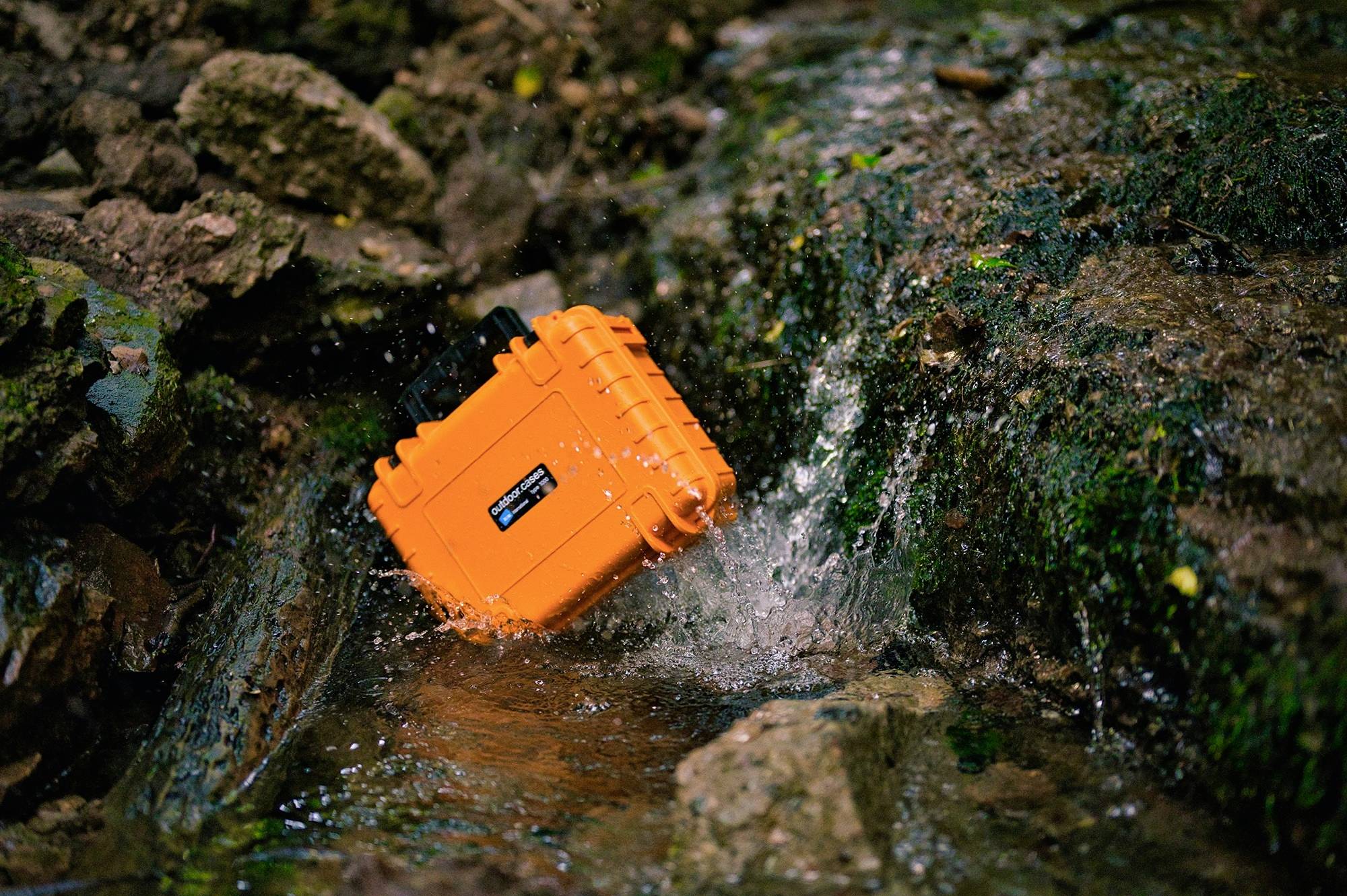 Une housse de protection orange imperméable repose dans un ruisseau aux eaux courantes et aux rochers, mettant en valeur sa robustesse et sa résistance.