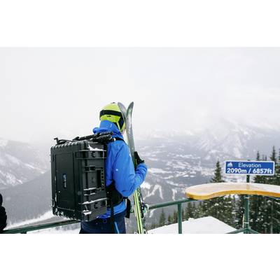 Une personne en tenue de ski, portant des skis sur le dos, se tient à un point de vue dans les montagnes. Un panneau indique 'Altitude 2090 m'.