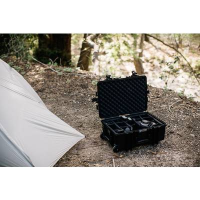 Une valise noire ouverte contenant des accessoires de photographie sur le sol forestier, à côté d'une tente dans une zone boisée.