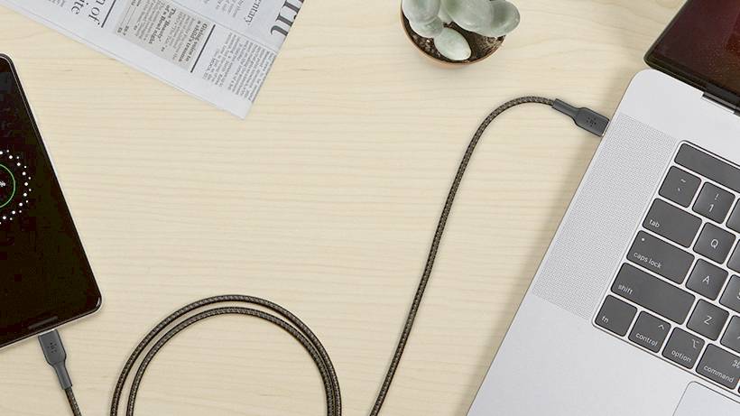 Smartphone branché à un câble de charge connecté à un ordinateur portable ; écran du smartphone affichant l'état de la charge.