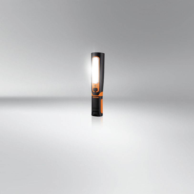 Une lampe de poche noir et orange est debout et brille intensément dans une pièce grise.
