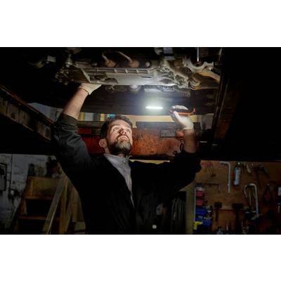 Mécanicien sous une voiture dans un atelier, concentré avec une lampe de poche à la main, en effectuant des réparations.