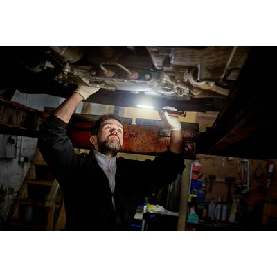 Un mécanicien travaille sous une voiture dans un atelier. Il utilise une lampe pour éclairer le dessous du véhicule.