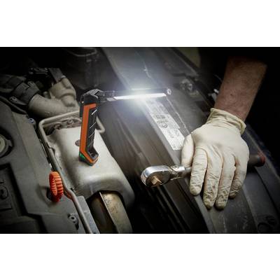 Une personne portant des gants répare un moteur dans une voiture. Une lampe de travail illumine la zone.