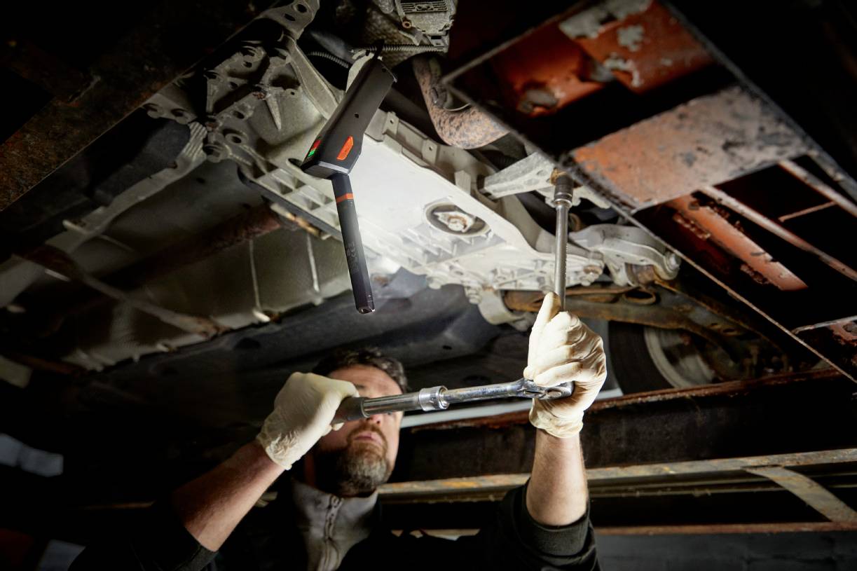 Un homme travaille sous une voiture, serrant des boulons avec une clé. Entretien automobile dans un atelier.
