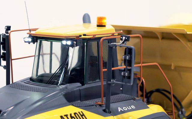 Chargeur sur pneus jaune avec signal de sécurité orange et grilles de protection, vue de la cabine et du godet dans un environnement lumineux.