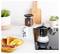 Un comptoir de cuisine avec une cafetière à espresso, une tasse de café, des œufs brouillés, du bacon, des toasts sur une assiette, et des plantes en pot.