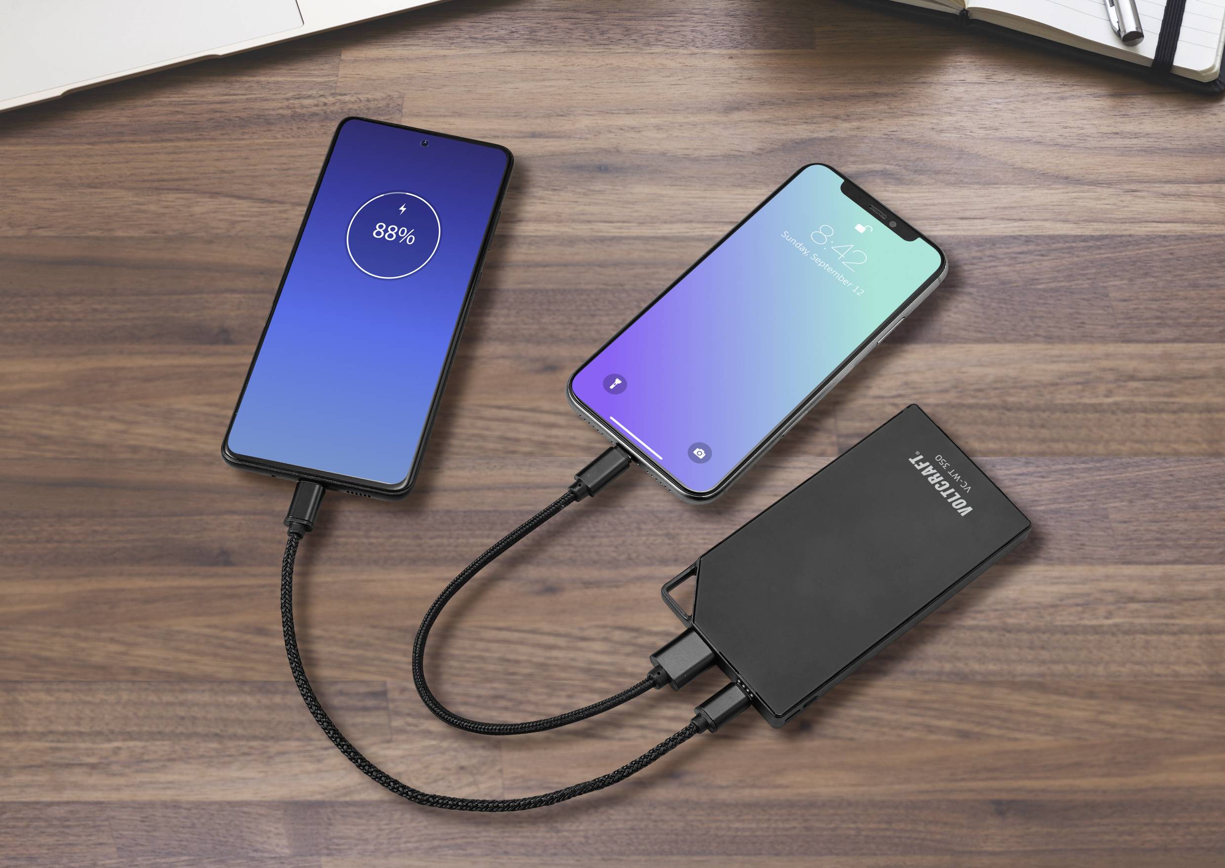 Deux smartphones sont en train de charger simultanément sur une batterie externe posée sur une table en bois ; l'un d'eux affiche 88% de batterie.