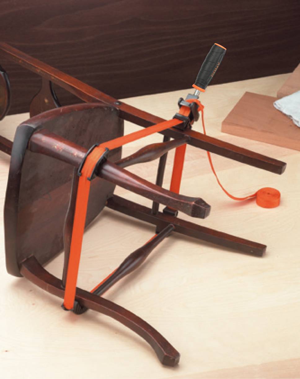 Une chaise retournée est fixée sur une table à l'aide d'une sangle de serrage. Elle est apparemment en cours de réparation ou d'assemblage.