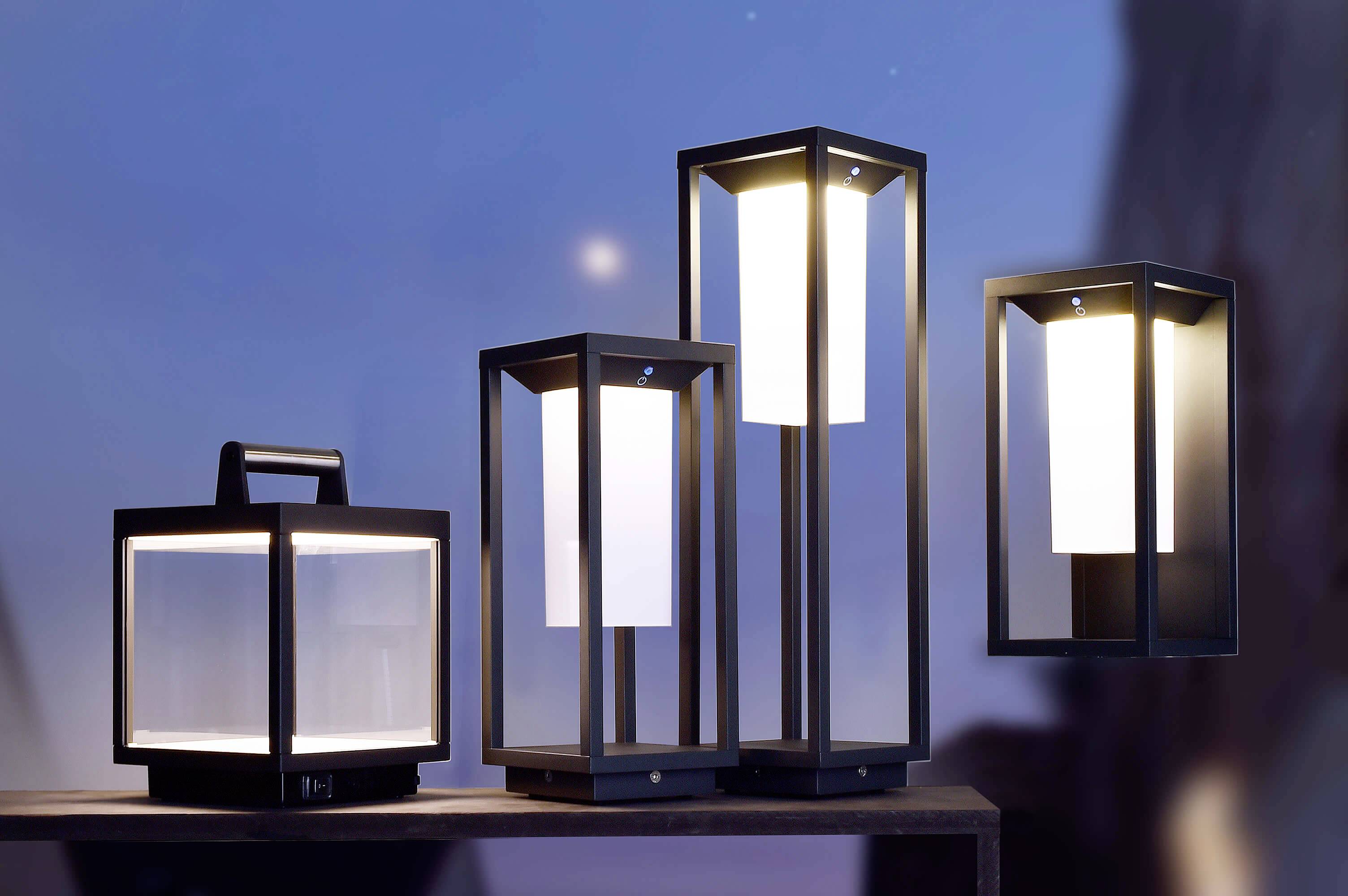 Différentes lanternes modernes en métal avec des cadres rectangulaires s'illuminent sur une table dans un environnement de soirée.