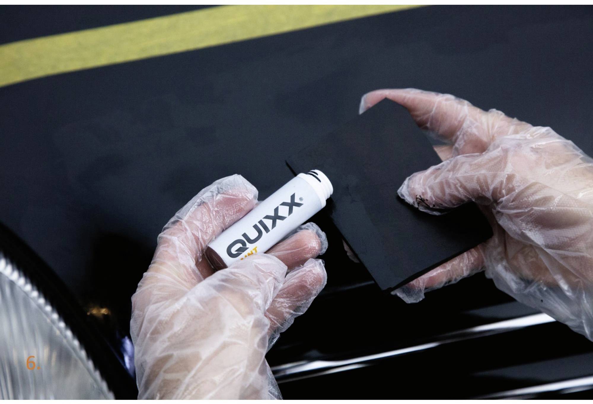 Une personne applique du polish Quixx sur la carrosserie d'une voiture à l'aide d'un chiffon. Les mains sont protégées par des gants.