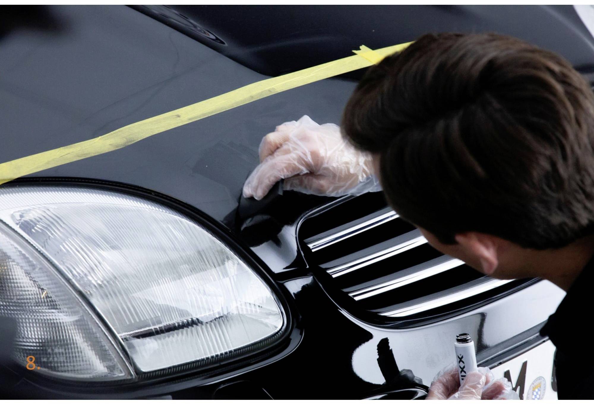 Une personne applique soigneusement du polish sur le capot d'une voiture noire, portant des gants, afin d'éliminer les rayures.